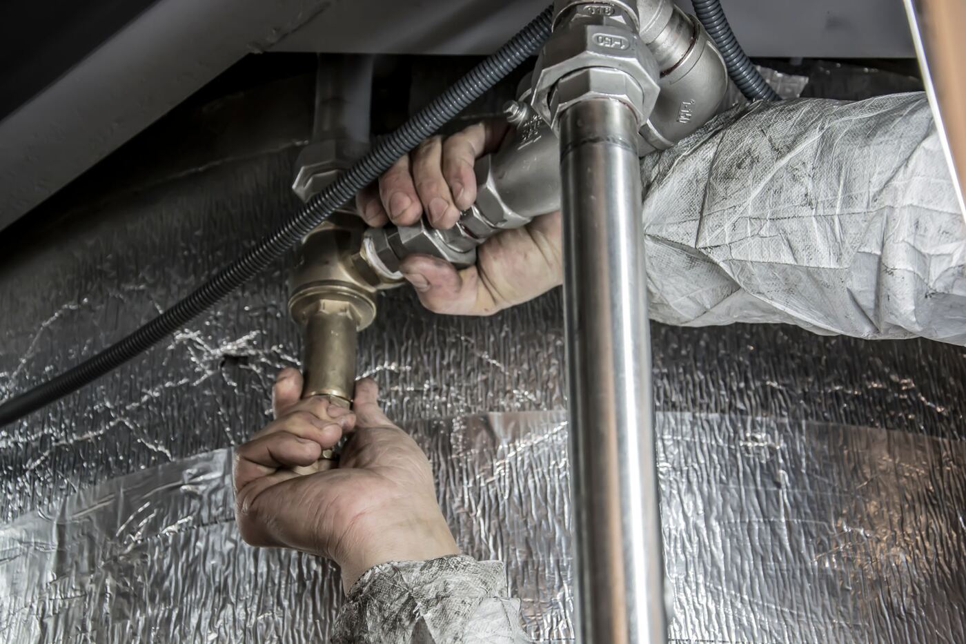 A tradesperson's hands working on pipework, unable to answer the phone